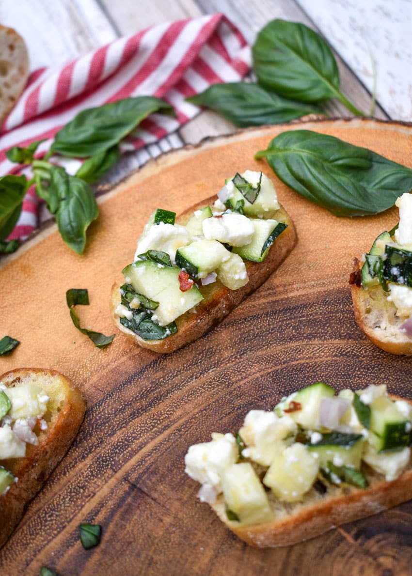 zucchini bruschetta on toasted baguette slices on a wooden cutting board