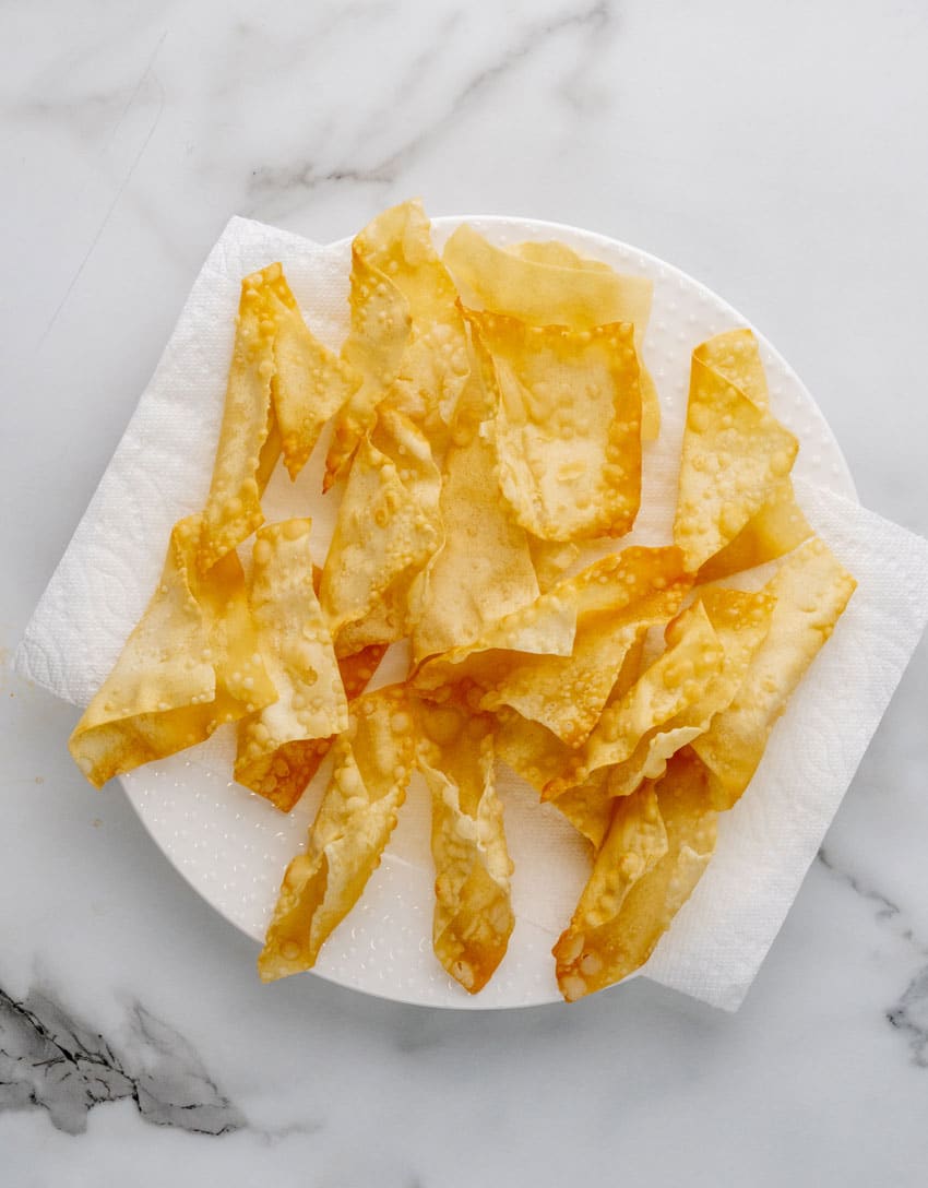 fried mini wonton wrapper taco shells draining on a paper towel lined plate