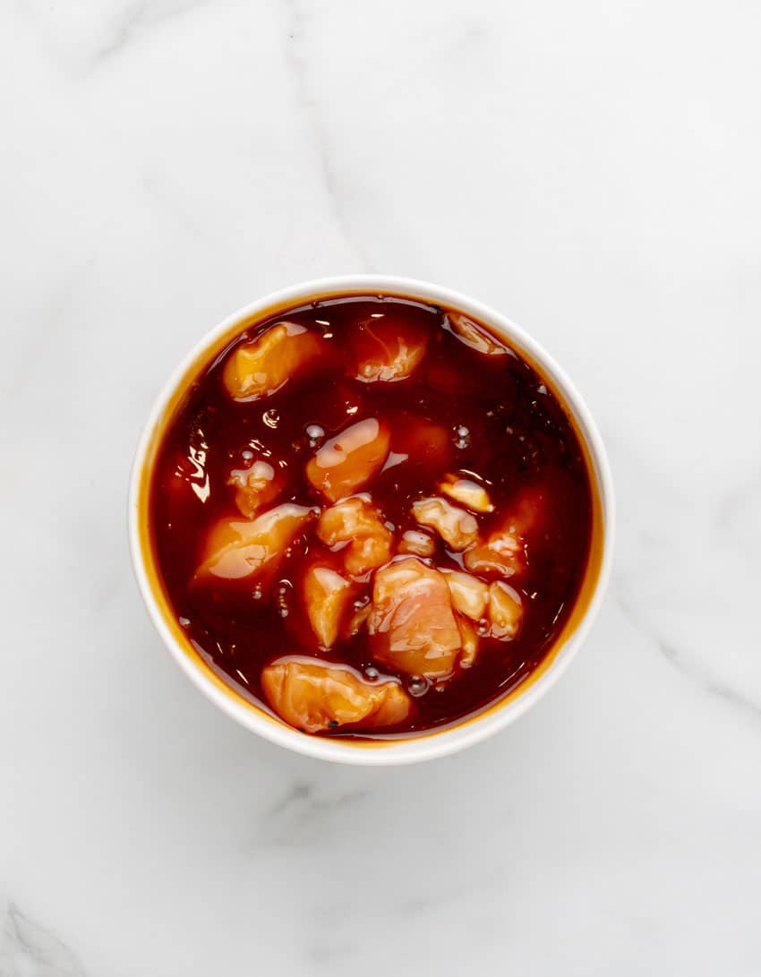 marinating chunks of chicken in a white bowl
