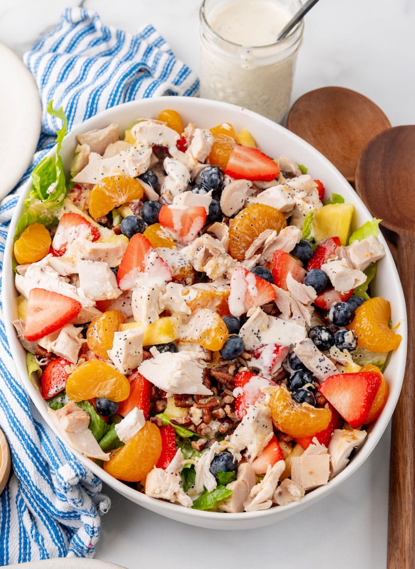 Copycat Panera strawberry poppyseed chicken salad in a white serving dish with wooden salad servers on the side