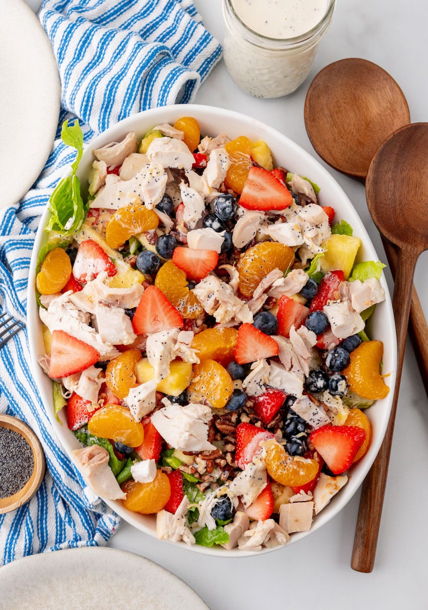 a homemade copycat Panera strawberry poppyseed chicken salad in a white serving dish with wooden salad servers on the side