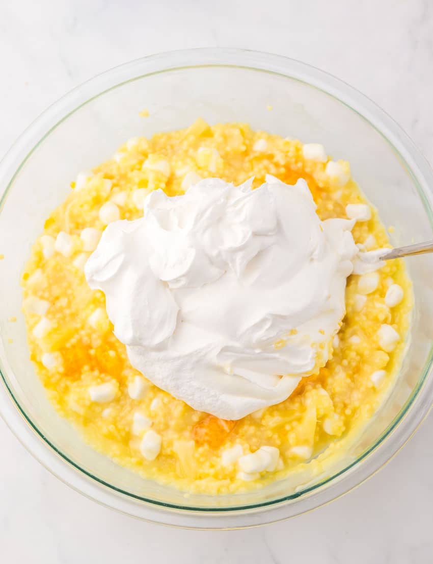 thawed cool whip being stirred into frog eye salad in a glass mixing bowl