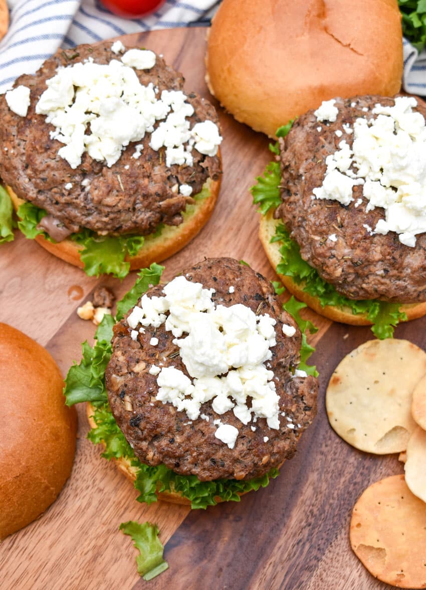 feta cheese topped gyro burgers on a wooden cutting board