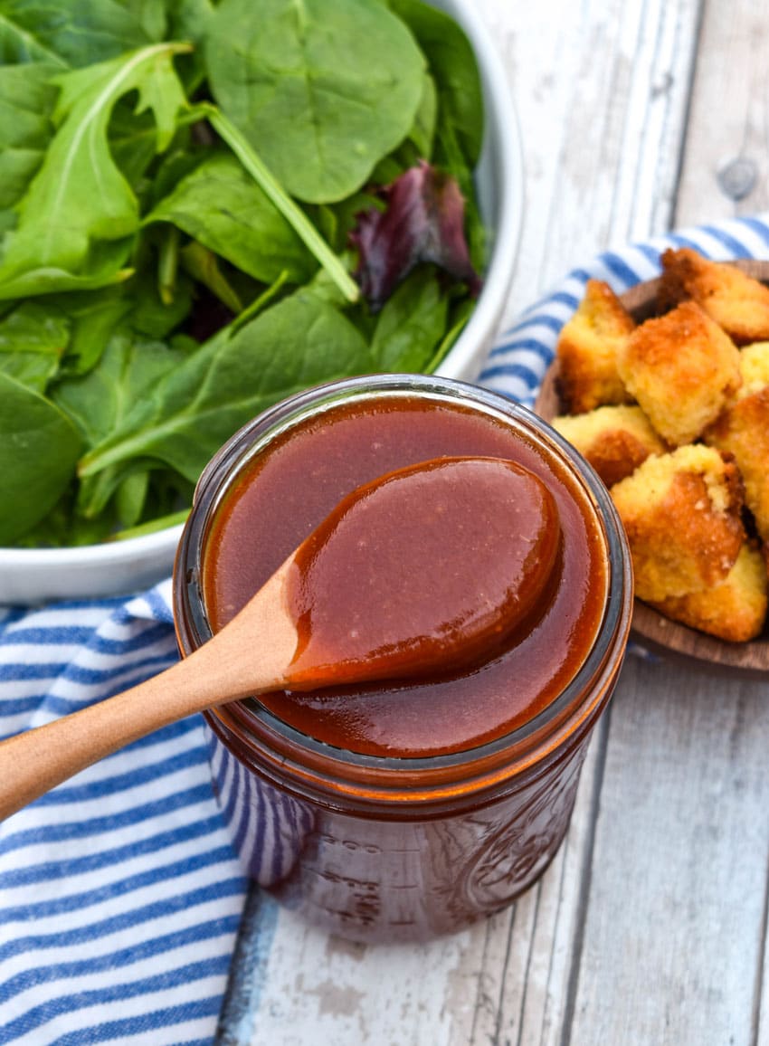 a wooden spoon scooping homemade catalina dressing out of a small glass jar