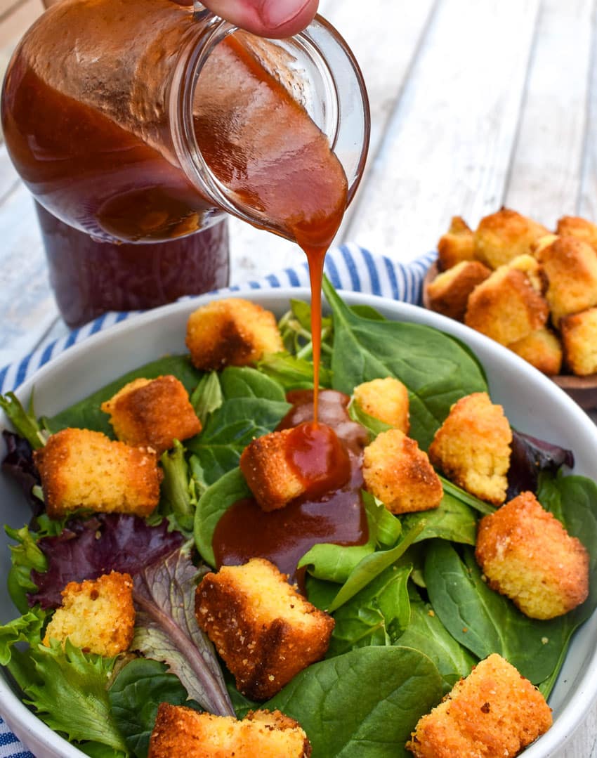 homemade catalina dressing being poured over a salad in a shallow white bowl