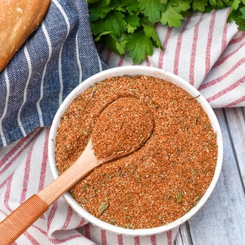 a wooden spoon scooping homemade creole seasoning out of a small white bowl