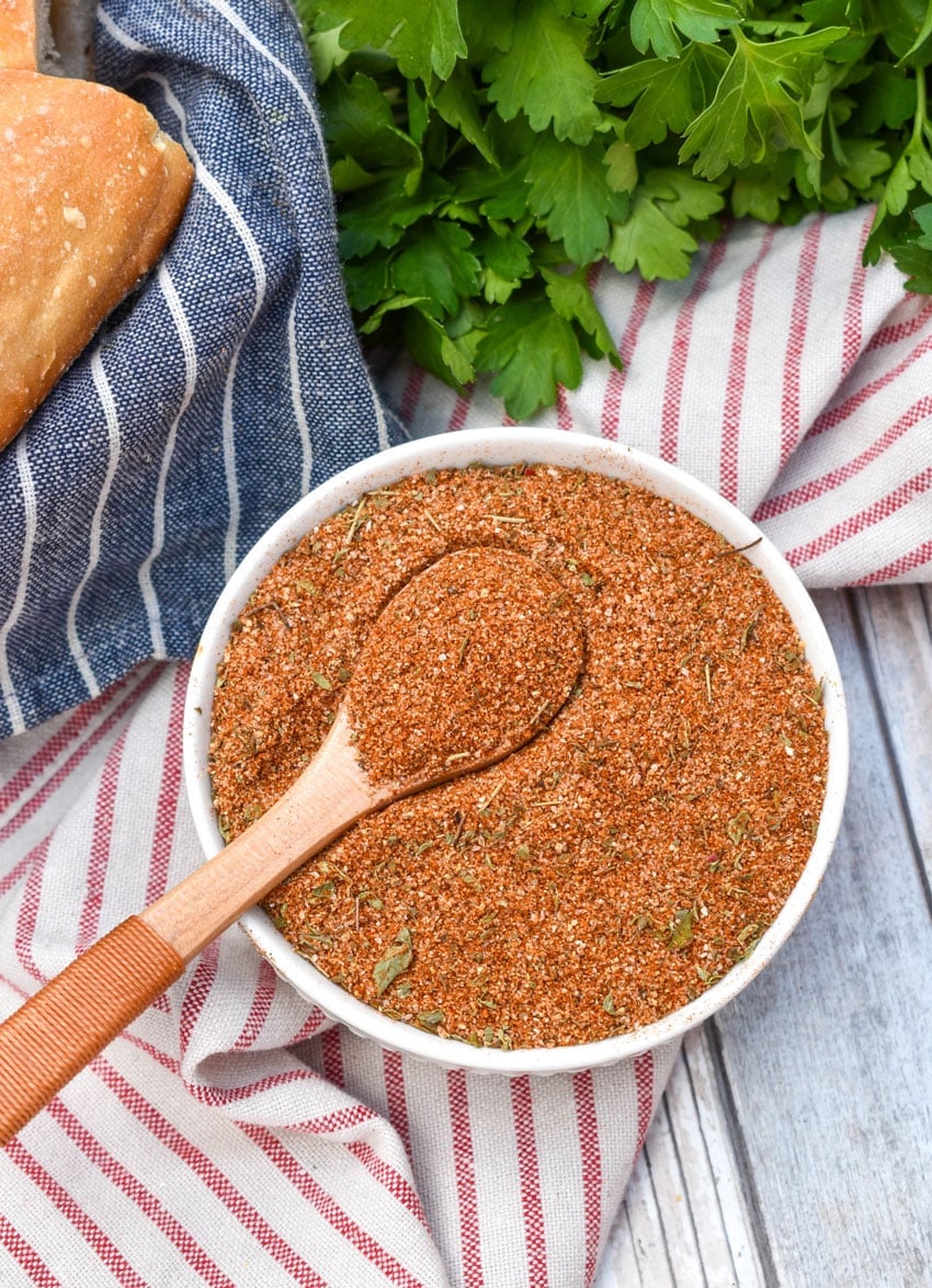 a wooden spoon scooping homemade creole seasoning out of a small white bowl