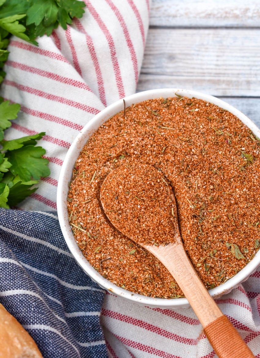 a wooden spoon scooping homemade creole seasoning out of a small white bowl