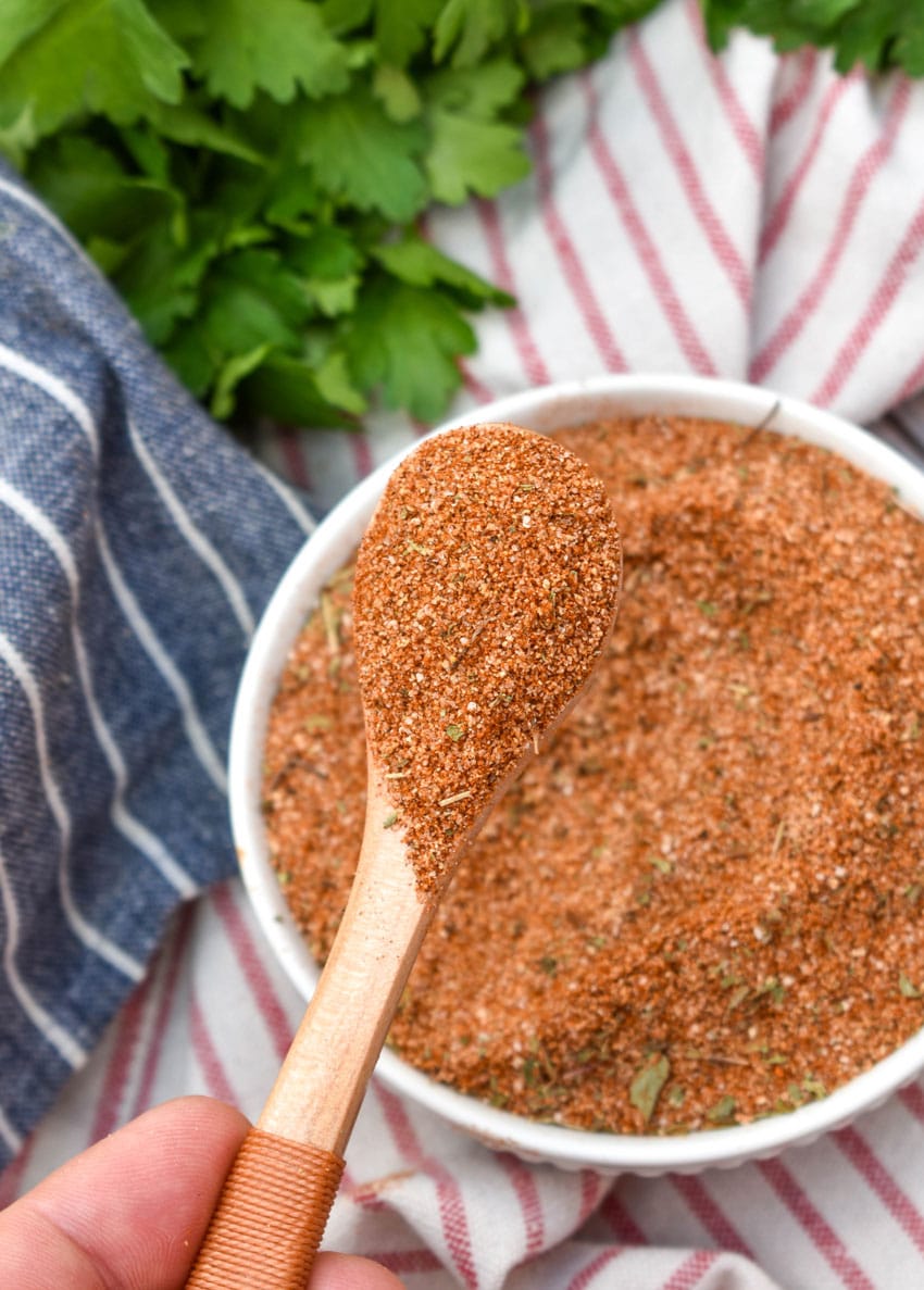 a wooden spoon scooping homemade creole seasoning out of a small white bowl