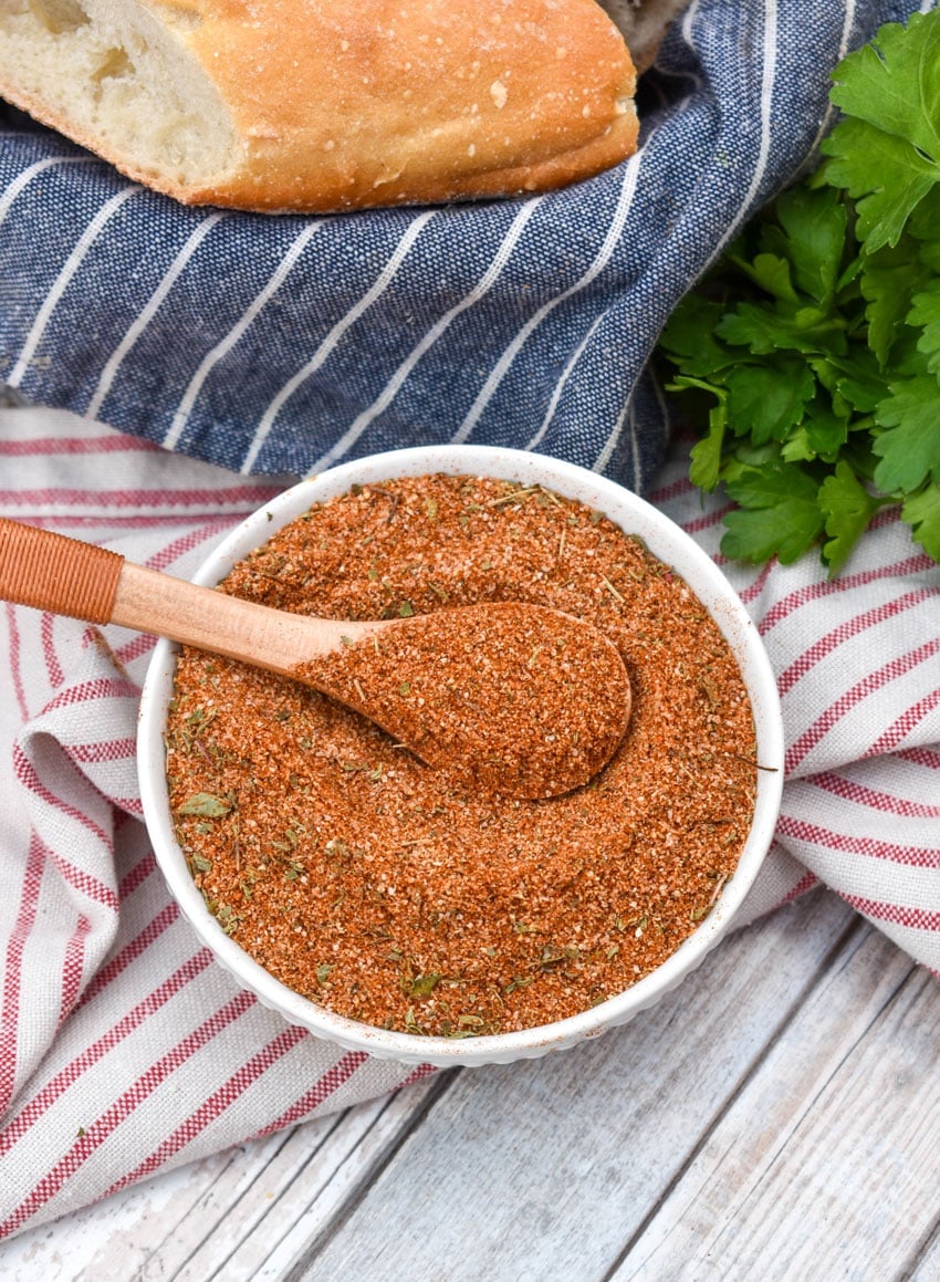 a wooden spoon scooping homemade creole seasoning out of a small white bowl