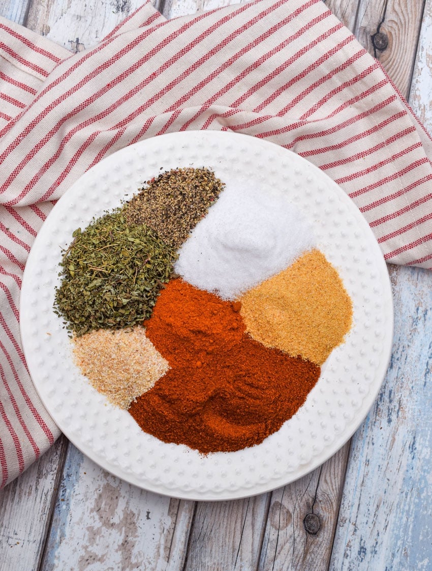 an overhead image showing the measured spices needed to make a batch of homemade creole seasoning on a small white plate