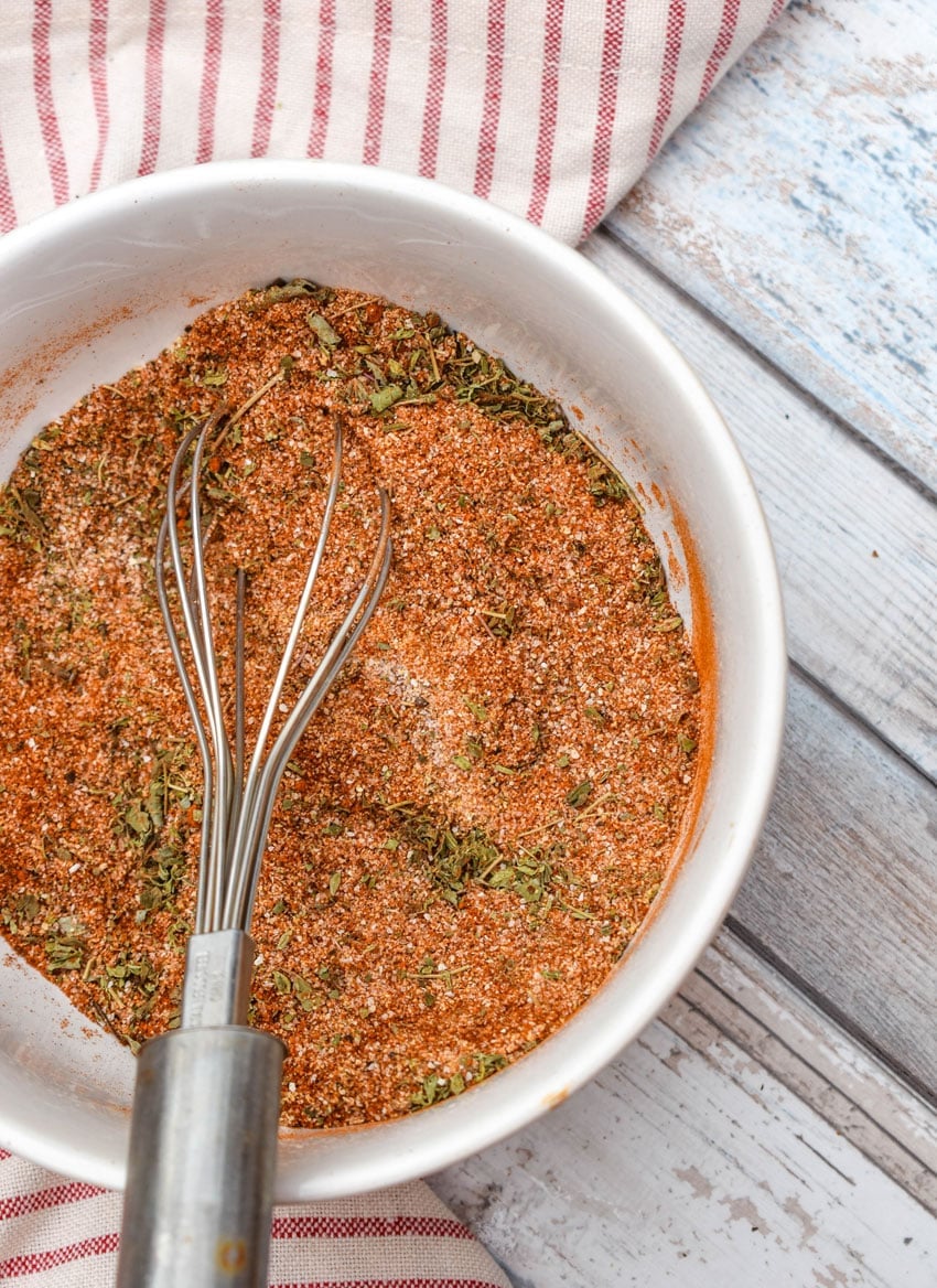 a wire whisk resting in a white bowl with a blend of homemade seasonings