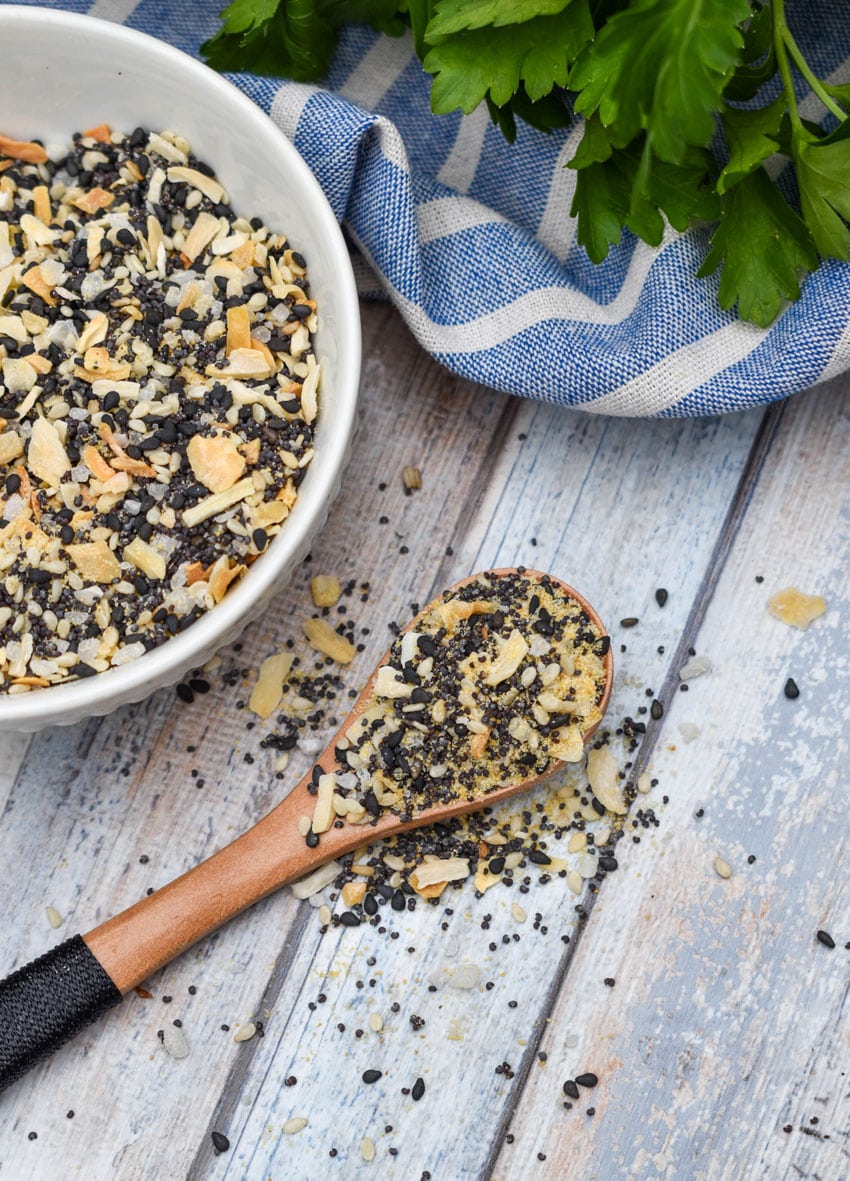 a small wooden spoon holding a scoop of homemade everything bagel seasoning resting on a wooden table