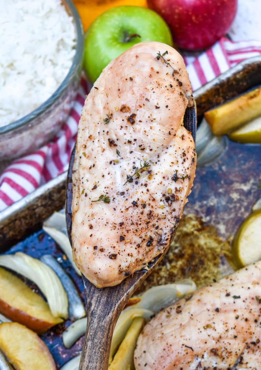a wooden spatula holding up a piece of roasted sheet pan chicken with apples