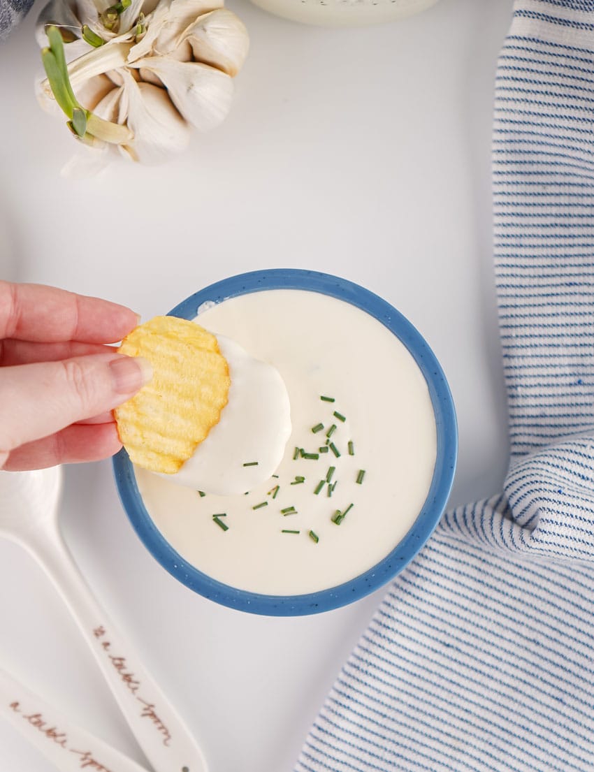 homemade sour cream in a small blue bowl with a potato chip resting on the edge