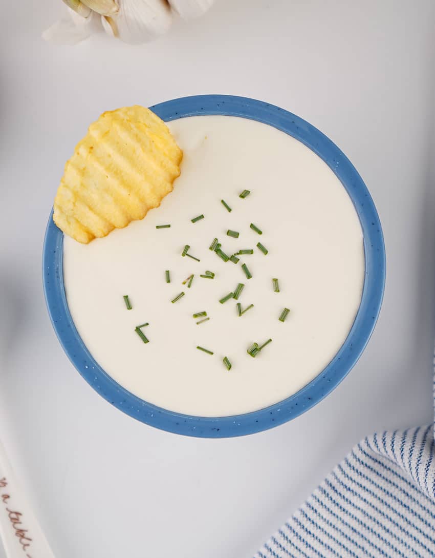 homemade sour cream in a small blue bowl with a potato chip resting on the edge