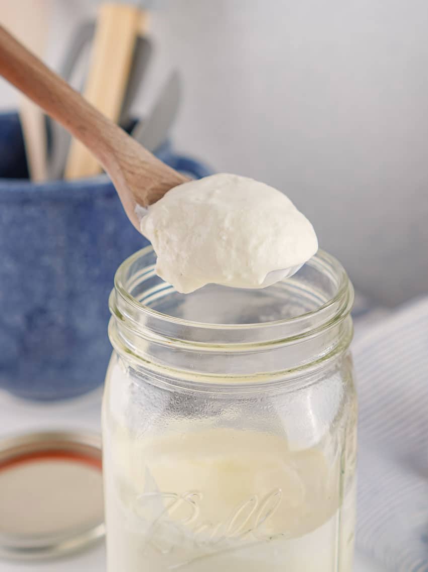 a wooden spoon holding up a scoop of homemade sour cream