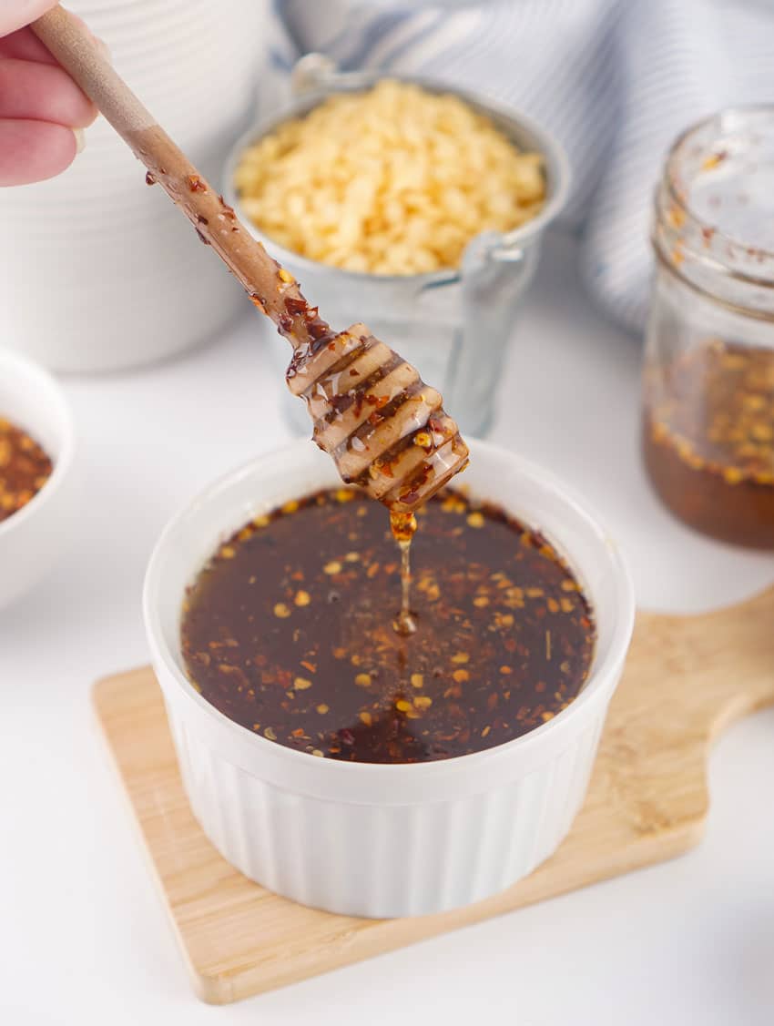 a wooden honey dipper dripping homemade hot honey into a small white bowl