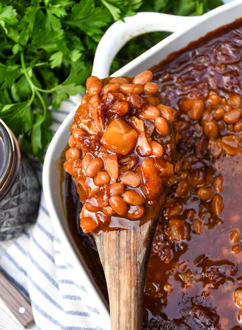 a wooden spoon holding up a scoop of homemade apple pie baked beans
