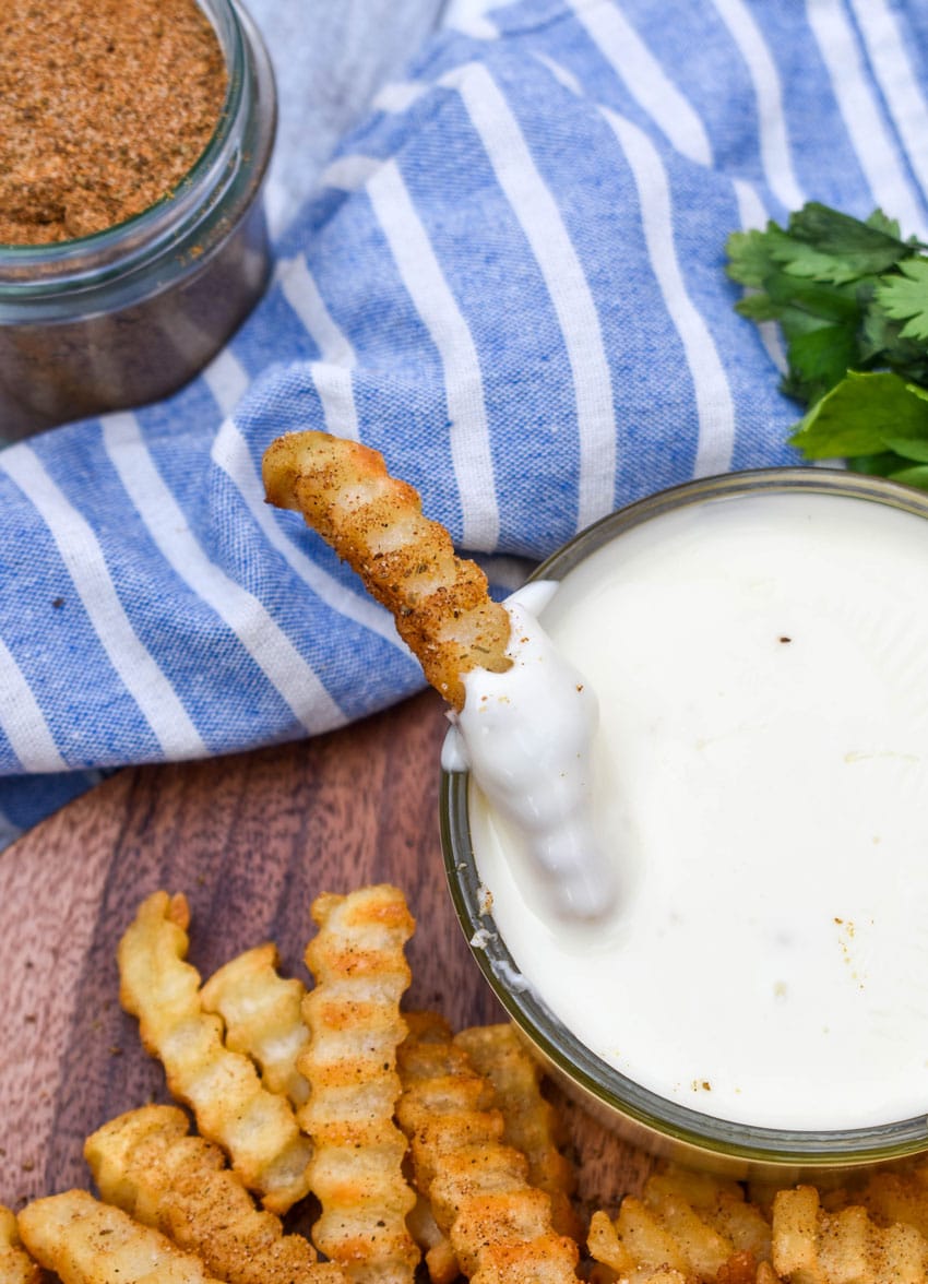 an old bay seasoned crispy crinkle french fry being dipped in a small bowl filled with creamy white cheese sauce