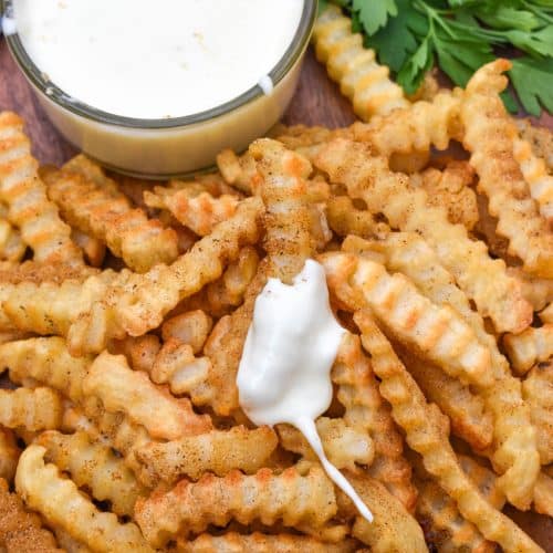 Copycat Chickie's & Pete’s crab fries on a wooden serving board with a small cup of creamy white cheese sauce on the side
