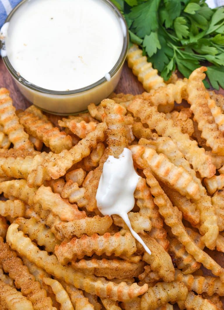 Copycat Chickie's & Pete’s crab fries on a wooden serving board with a small cup of creamy white cheese sauce on the side