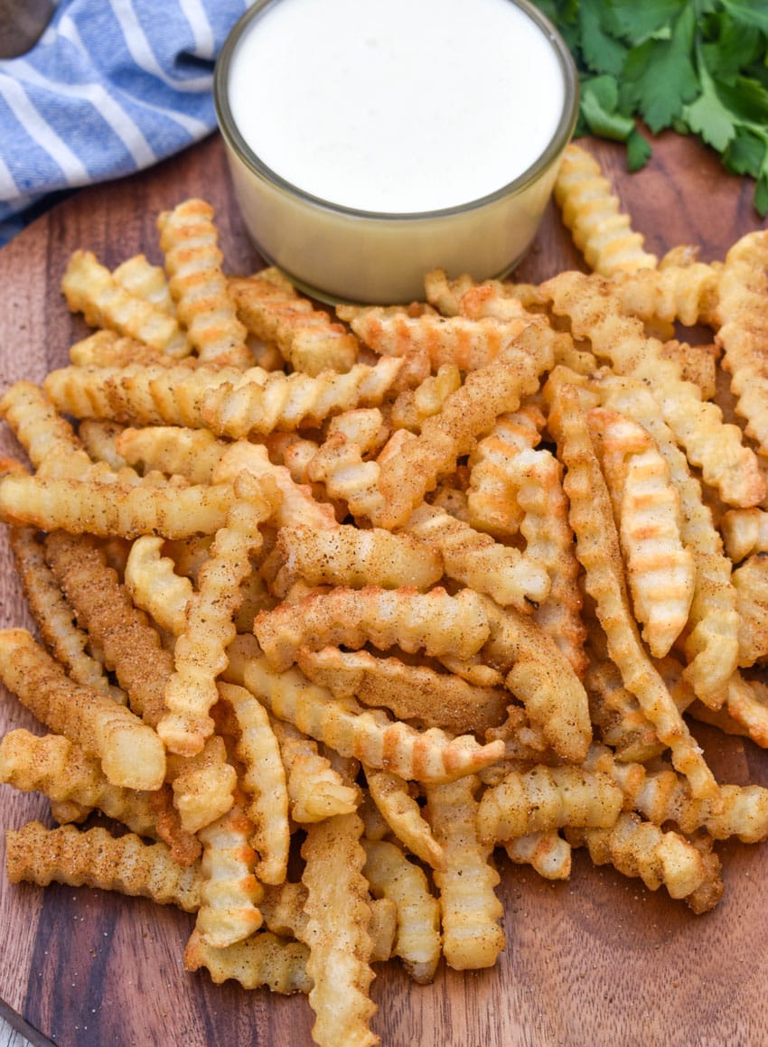 Copycat Chickie's & Pete’s crab fries on a wooden serving board with a small cup of creamy white cheese sauce on the side