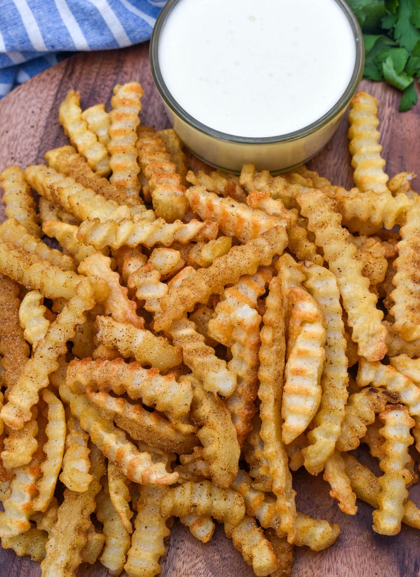 Copycat Chickie's & Pete’s crab fries on a wooden serving board with a small cup of creamy white cheese sauce on the side