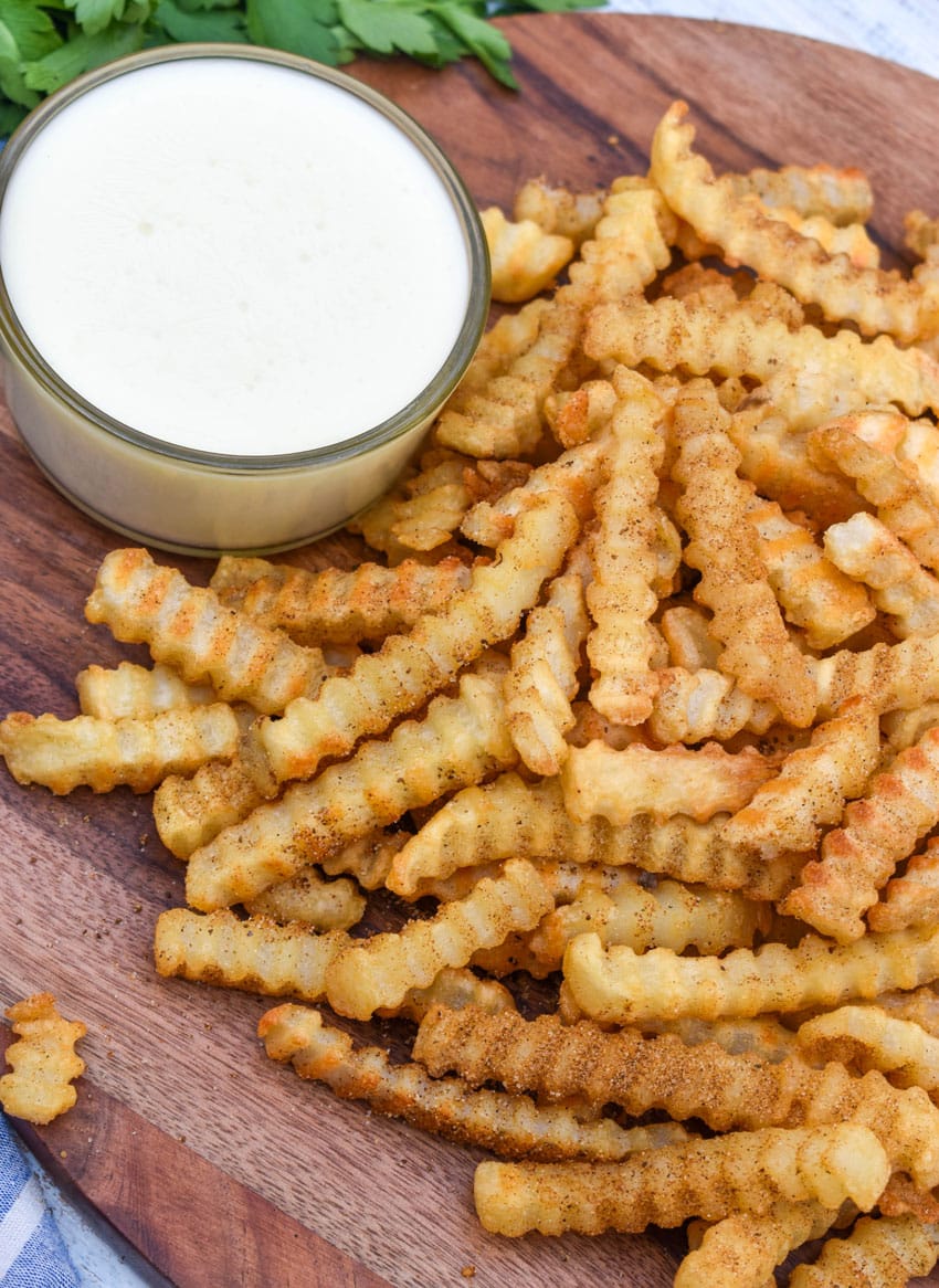 Copycat Chickie's & Pete’s crab fries on a wooden serving board with a small cup of creamy white cheese sauce on the side