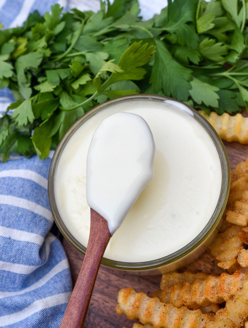 a small wooden spoon holding up a scoop of homemade white cheese sauce