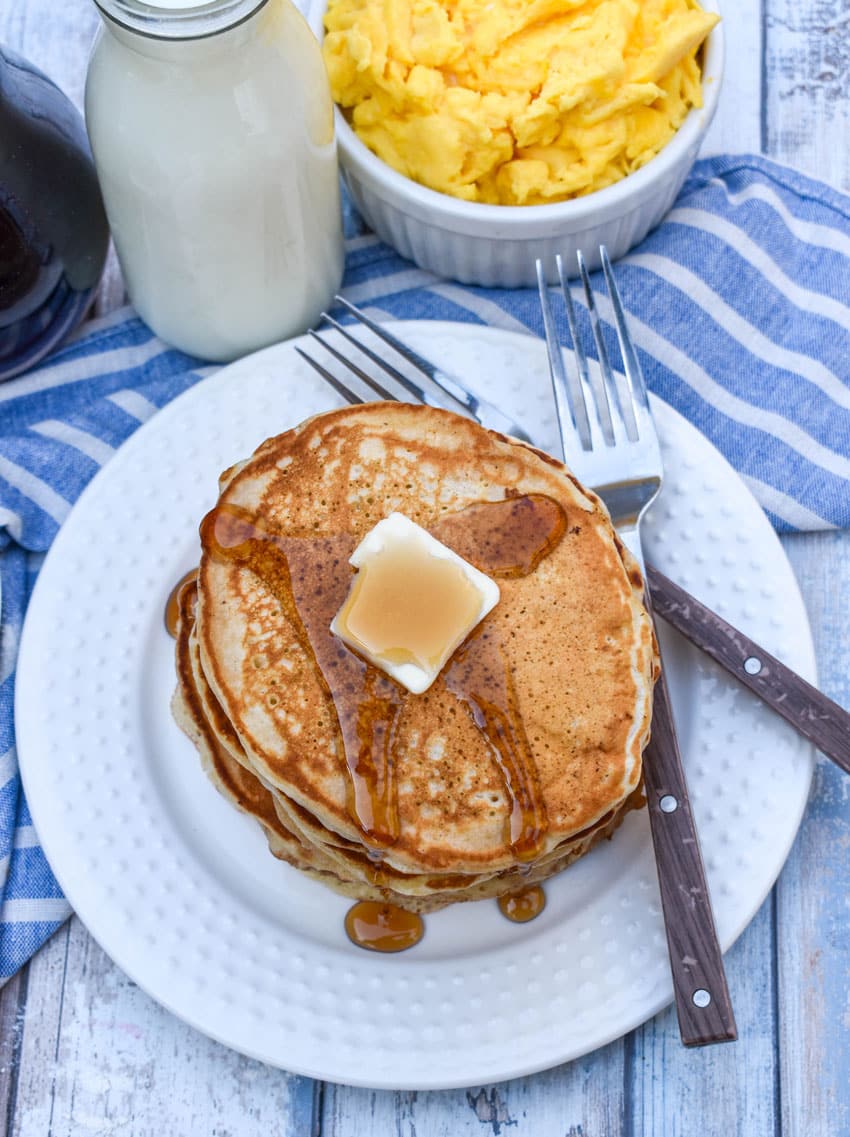 a small stack of homemade pancakes topped with syrup and a pat of butter on a small white plate
