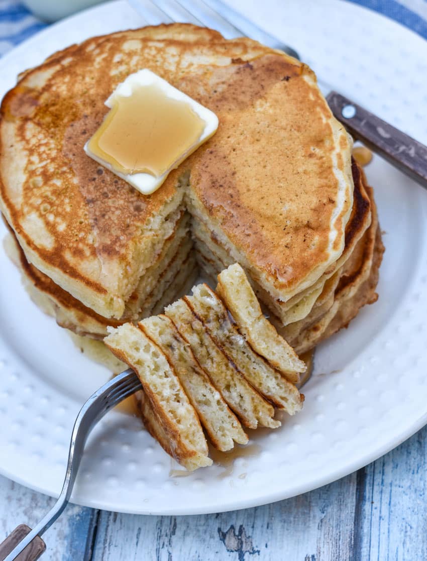 a small stack of homemade pancakes topped with syrup and a pat of butter on a small white plate