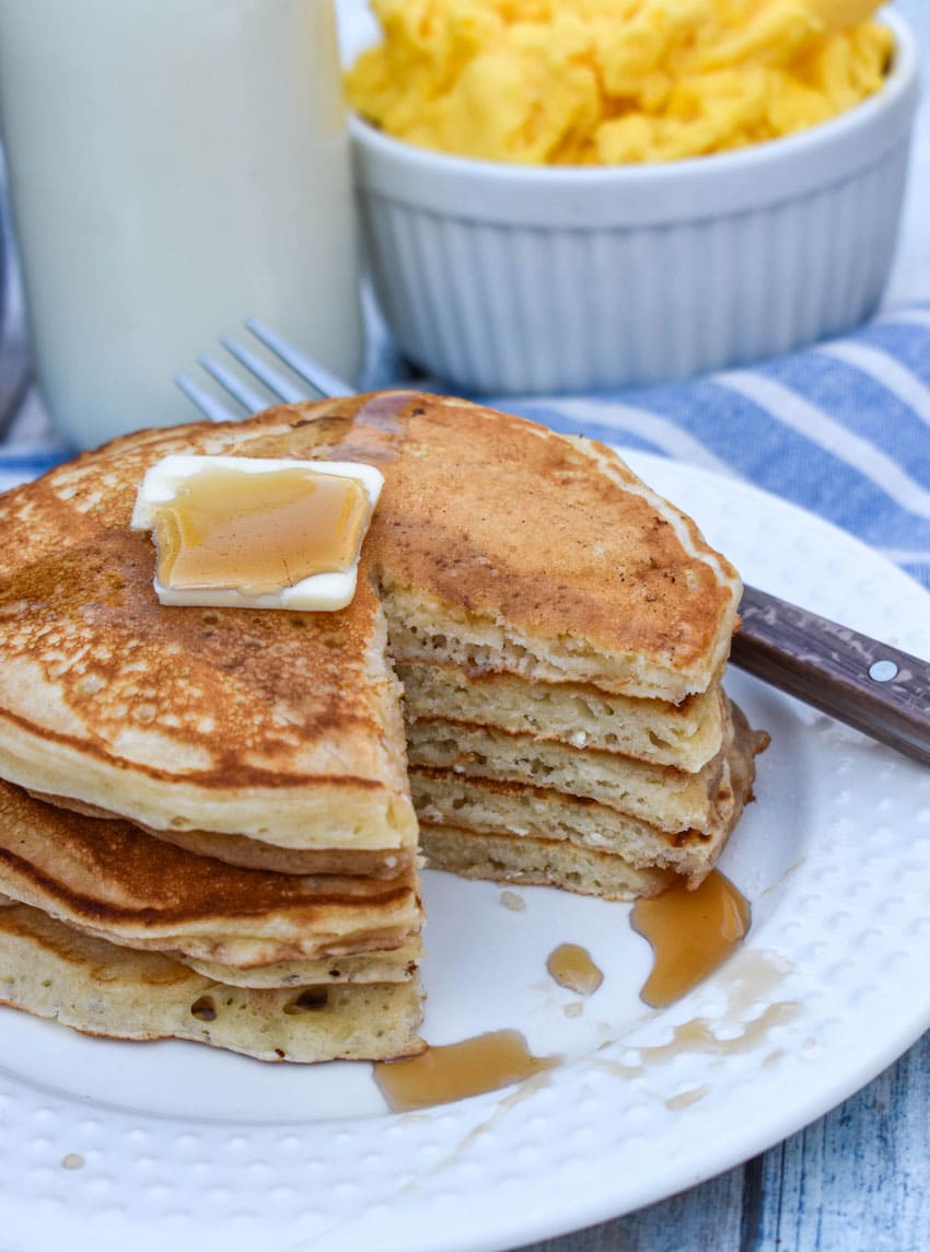 a small stack of homemade pancakes topped with syrup and a pat of butter on a small white plate