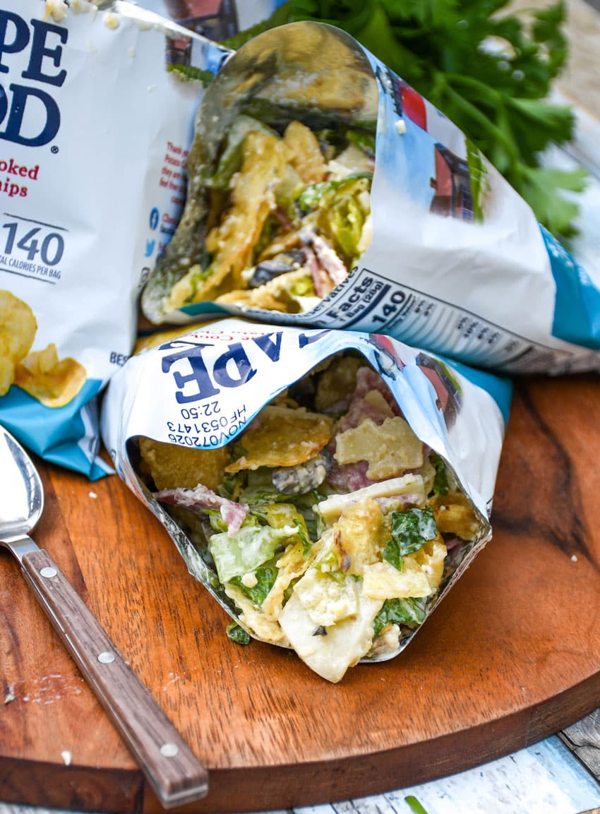 a group of prepared chip bag sandwiches on a wooden serving board with fresh herbs in the background