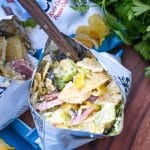 a group of prepared chip bag sandwiches on a wooden serving board with fresh herbs in the background