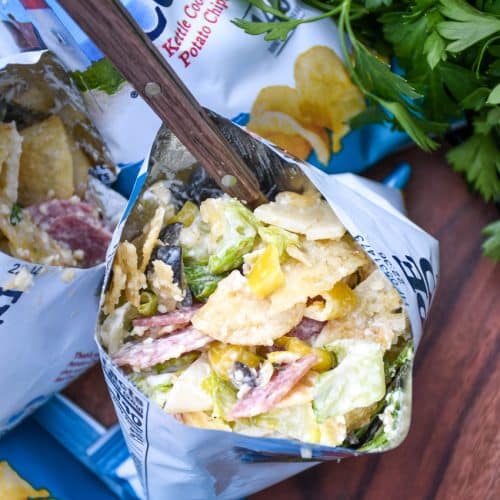 a group of prepared chip bag sandwiches on a wooden serving board with fresh herbs in the background