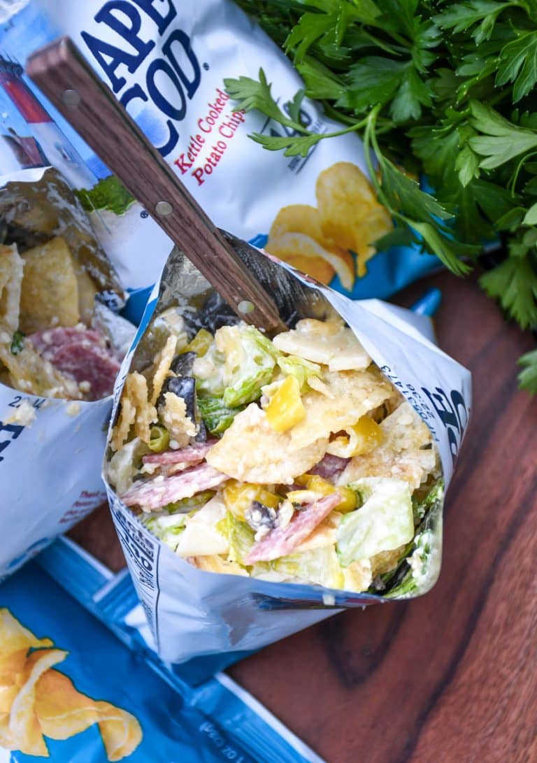a group of prepared chip bag sandwiches on a wooden serving board with fresh herbs in the background