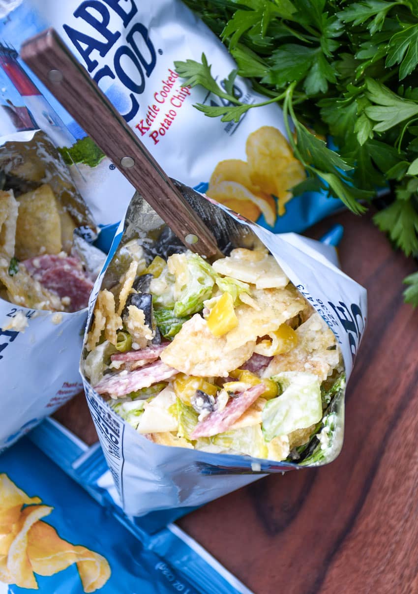 a group of prepared chip bag sandwiches on a wooden serving board with fresh herbs in the background