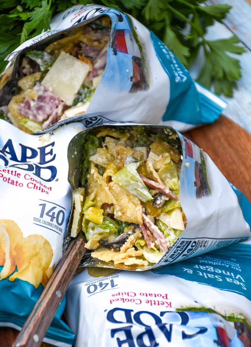 a group of prepared chip bag sandwiches on a wooden serving board with fresh herbs in the background