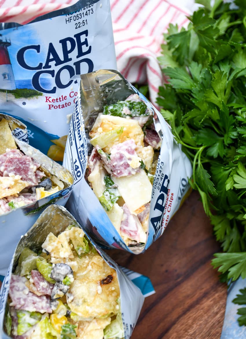 a group of prepared chip bag sandwiches on a wooden serving board with fresh herbs in the background