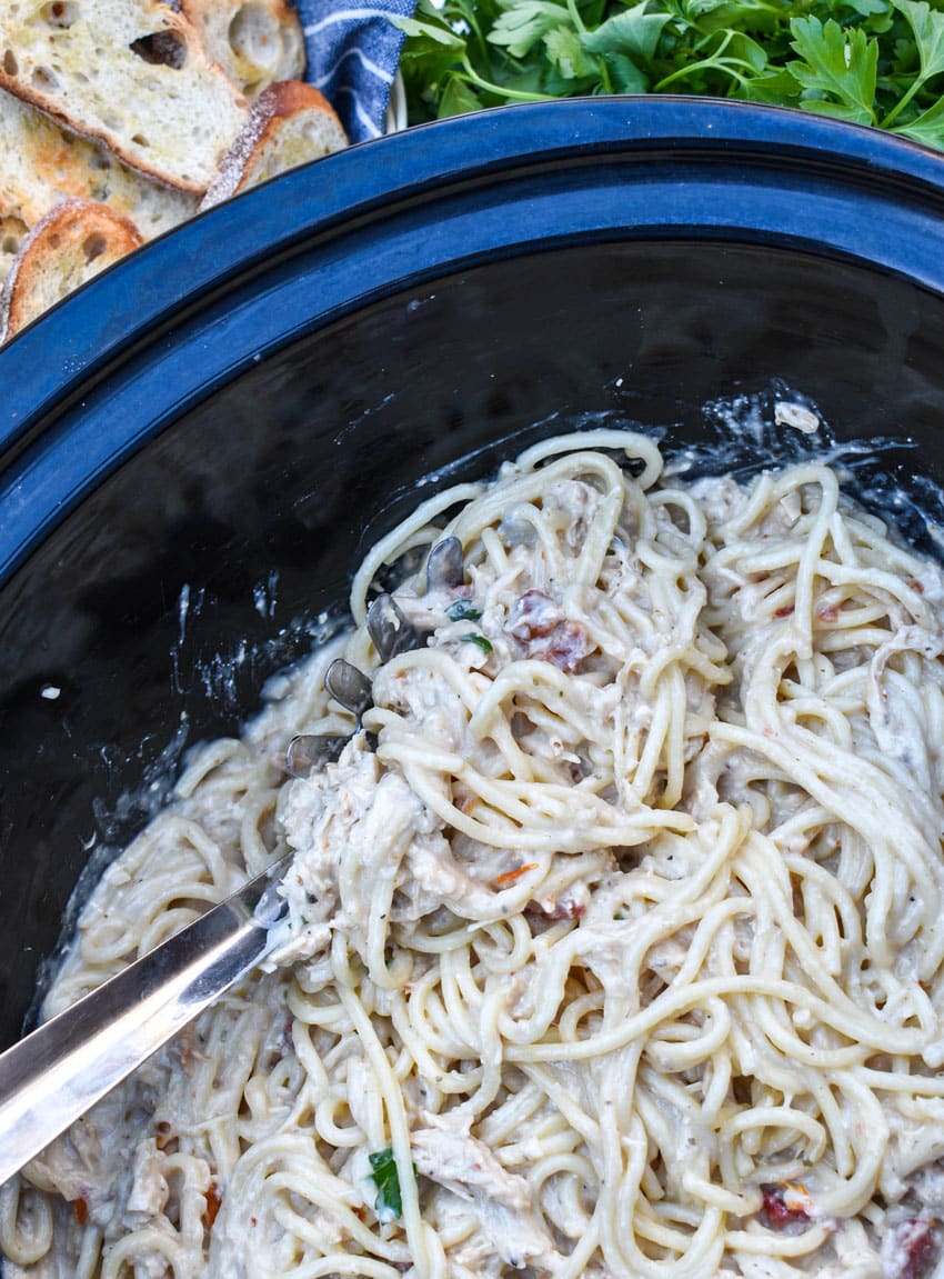 a silver spoon scooping creamy marry me chicken spaghetti out of the black bowl of a slow cooker