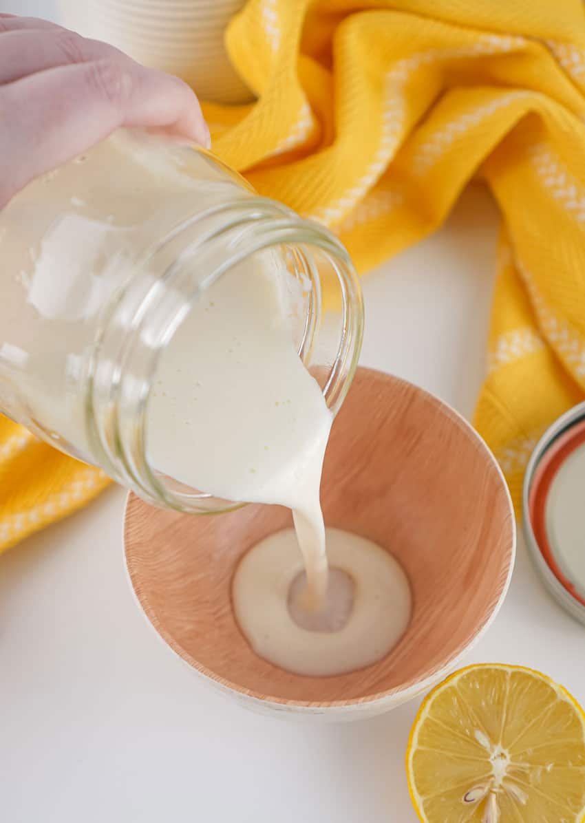homemade buttermilk being poured from a glass mason jar into a small wooden prep bowl