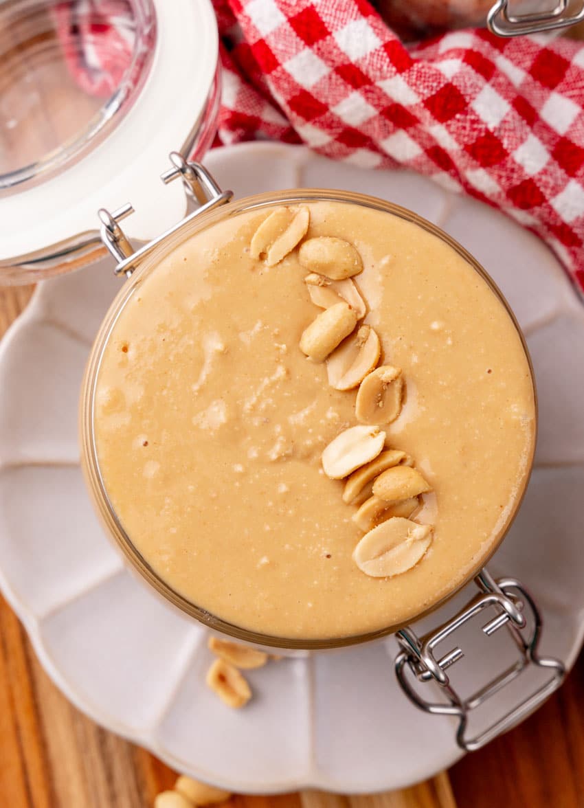homemade peanut butter in a small glass jar sitting on a small white plate