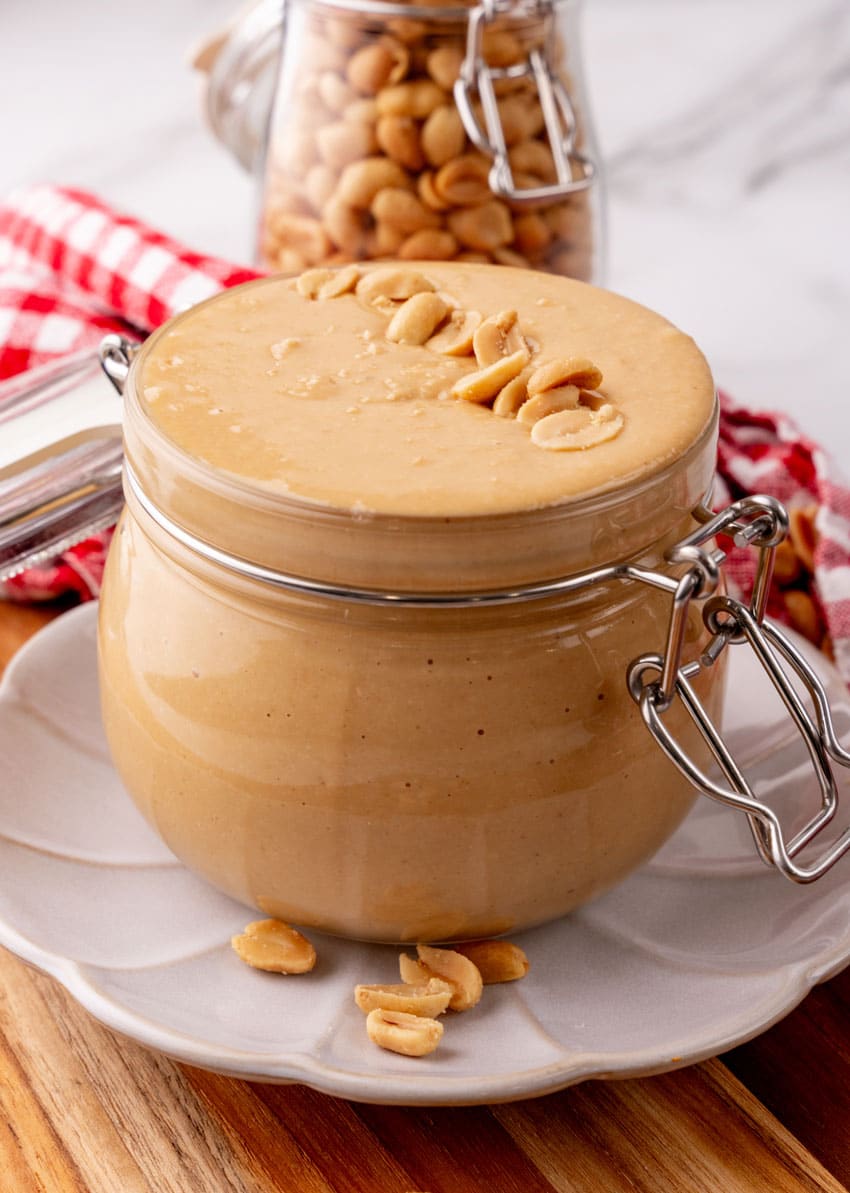 homemade peanut butter in a small glass jar sitting on a small white plate