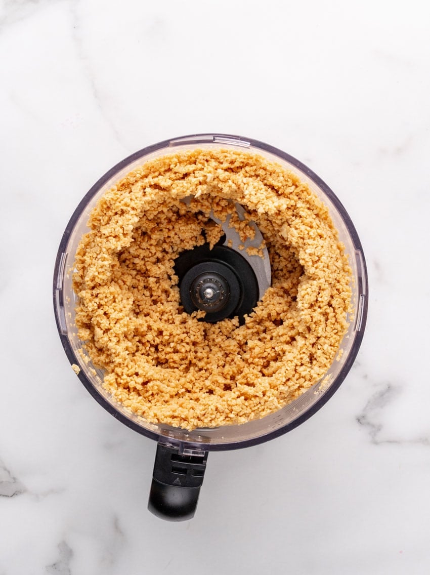 peanuts being ground up in the bowl of a food processor fitted with the blade attachment