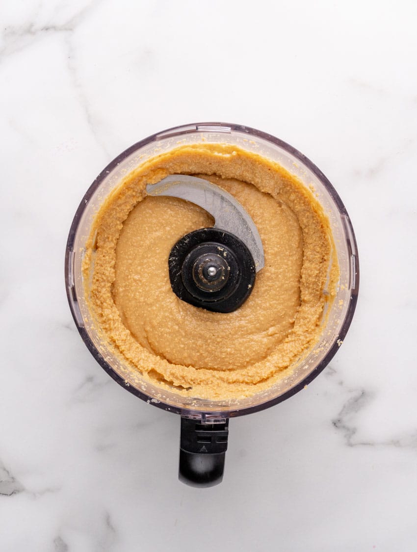 homemade creamy peanut butter being made in the bowl of a food processor fitted with the blade attachment
