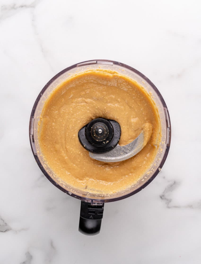 homemade creamy peanut butter being made in the bowl of a food processor fitted with the blade attachment