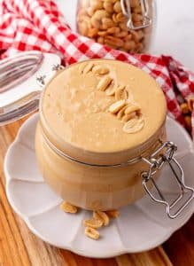 homemade peanut butter in a small glass jar sitting on a small white plate
