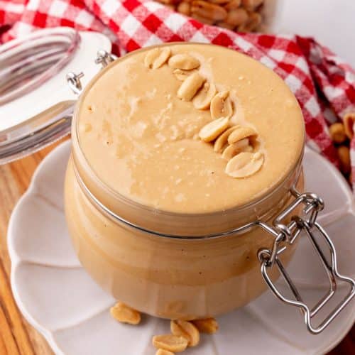 homemade peanut butter in a small glass jar sitting on a small white plate