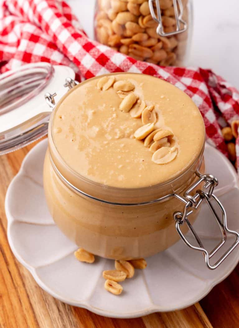 homemade peanut butter in a small glass jar sitting on a small white plate